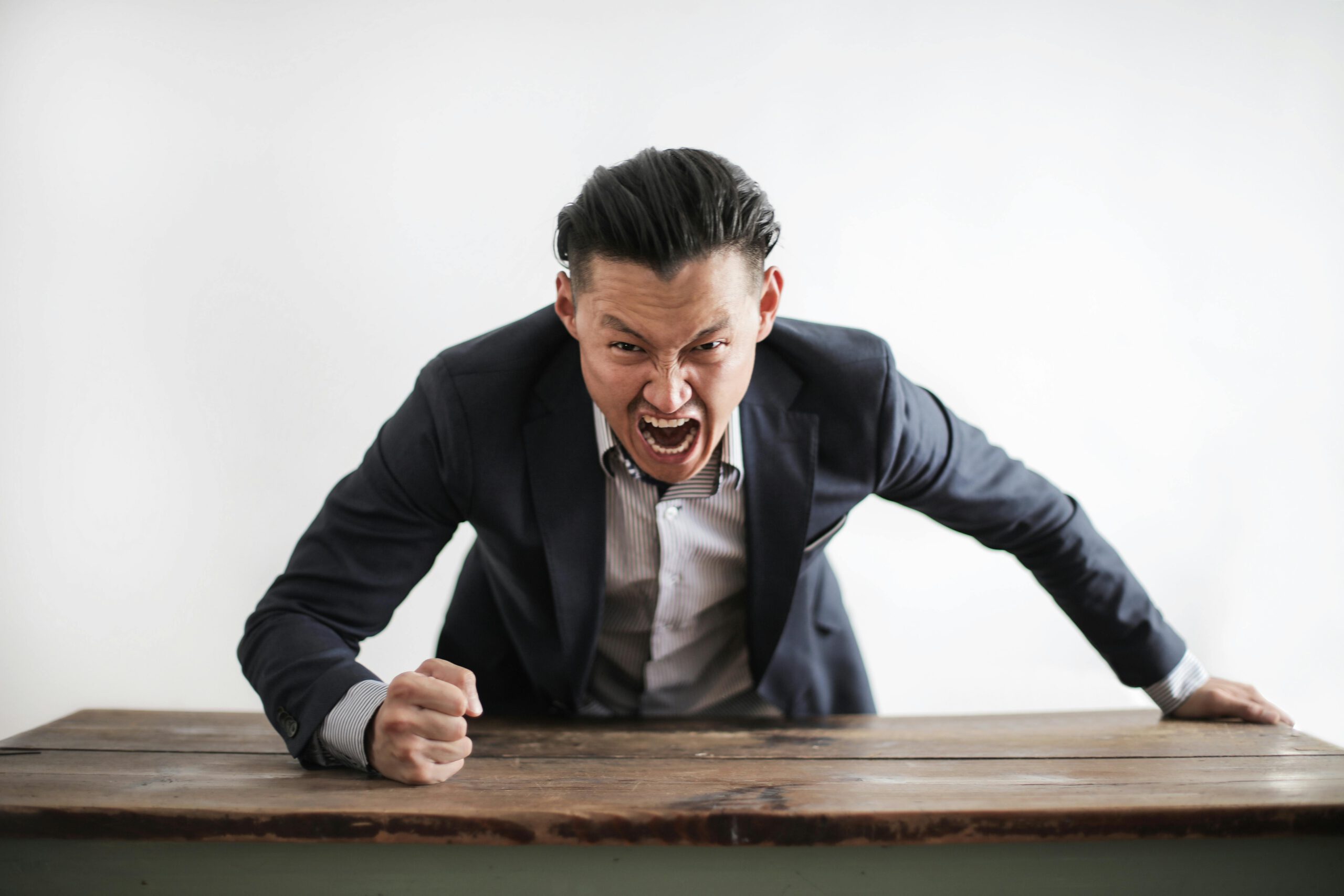 Illustration of Expressive angry businessman in formal suit looking at camera and screaming with madness while hitting desk with fist for the article titled Host a Thrilling Anti-Valentine's Day 2024 Party: Alternative Celebration Ideas for Singles and Friends photographed by Andrea Piacquadio