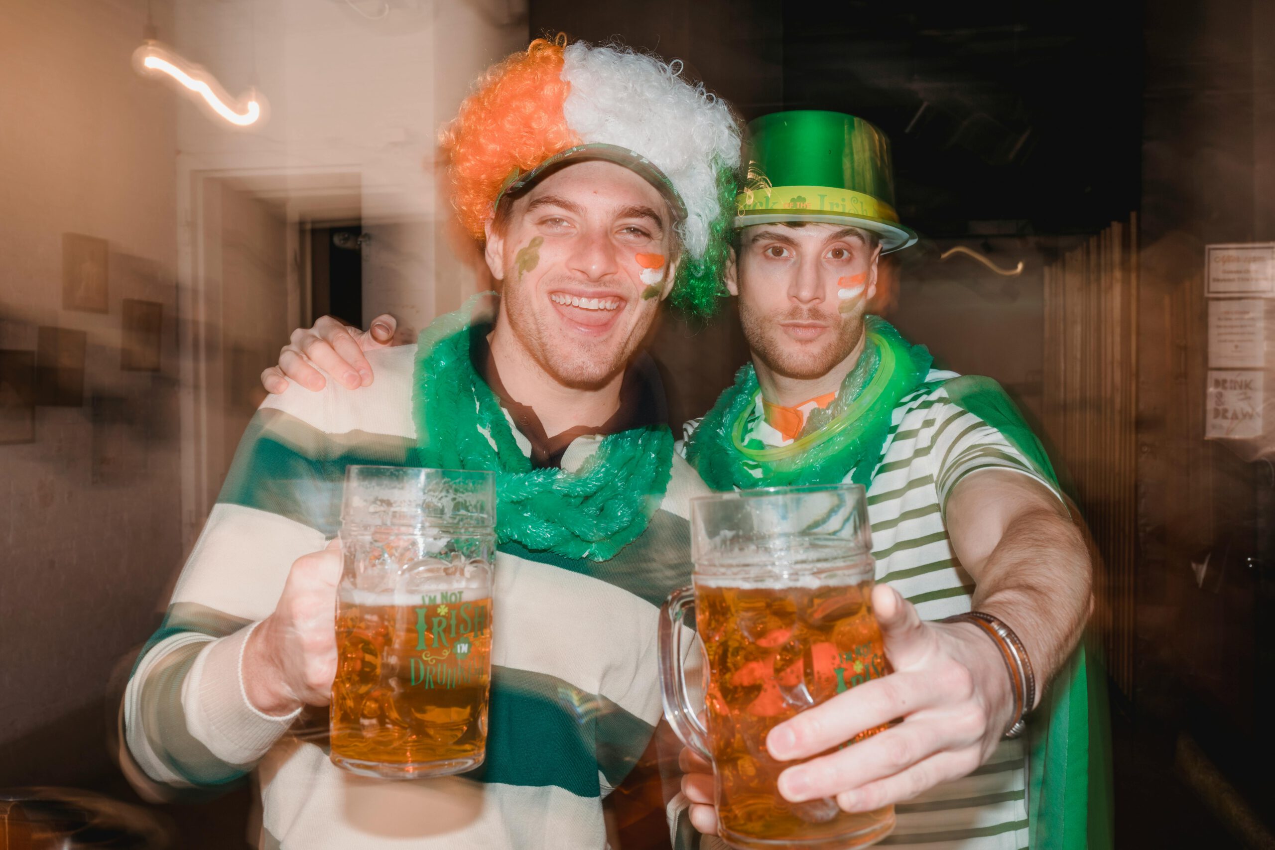Illustration of Happy men with glasses of cold beer in festive St Patricks day outfits looking at camera together for the article titled St. Patrick's Day 2024: Perfect Playlist and Games to Uplift Your Irish Themed Party photographed by Laura Tancredi