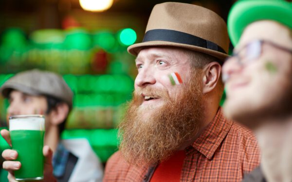Featured image for the article "Unveiling St. Patrick’s Day Magic 2024: Your Complete Guide to Dressing, Hosting, and Partying like the Irish". showing Man in Fedora Hat With Drink in Hand