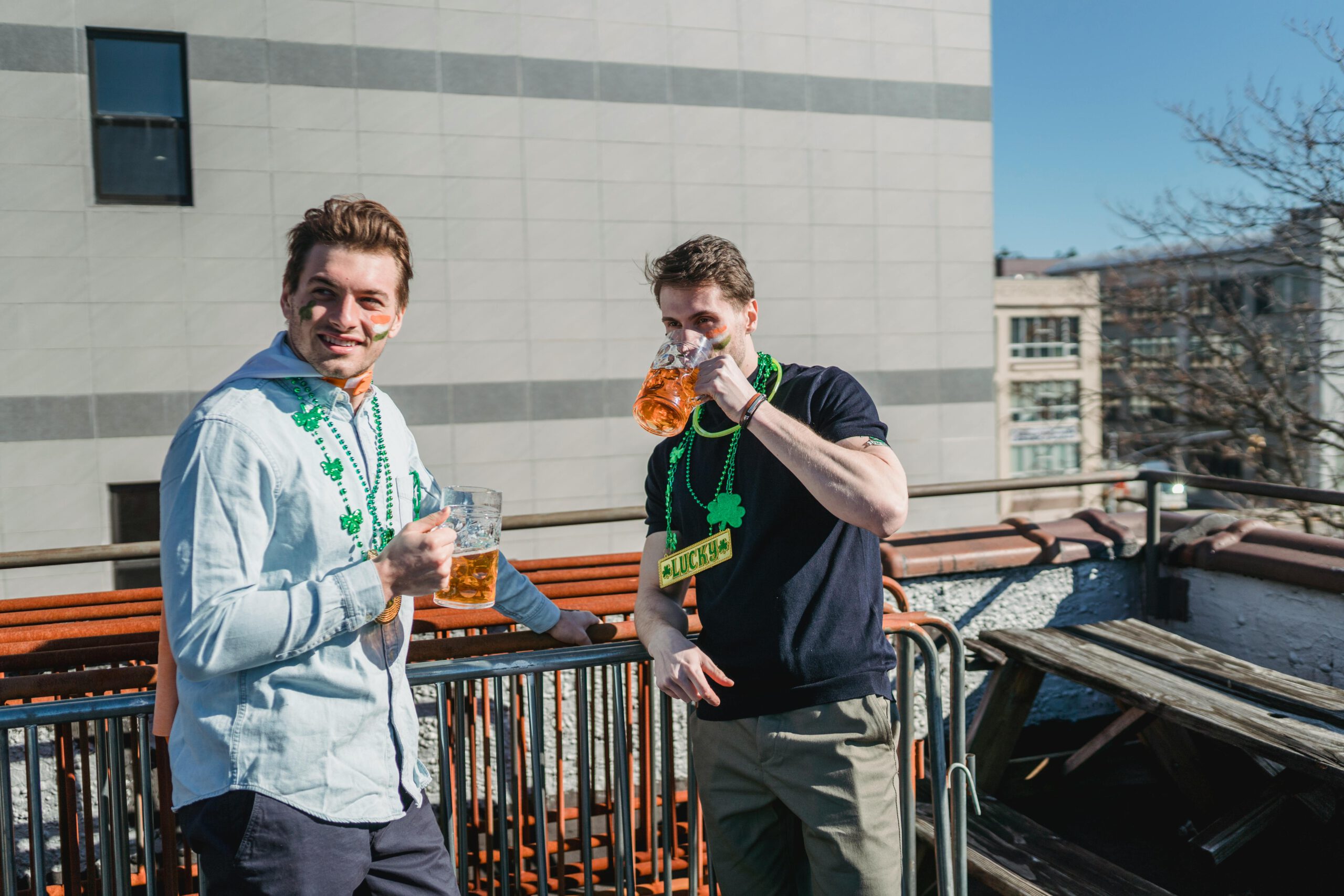 Illustration of Happy young male millennials in casual clothes and clover necklaces drinking glasses of beer while celebrating Feast of Saint Patrick on sunny day on terrace for the article titled Unveiling St. Patrick's Day Magic 2024: Your Complete Guide to Dressing, Hosting, and Partying like the Irish photographed by Laura Tancredi