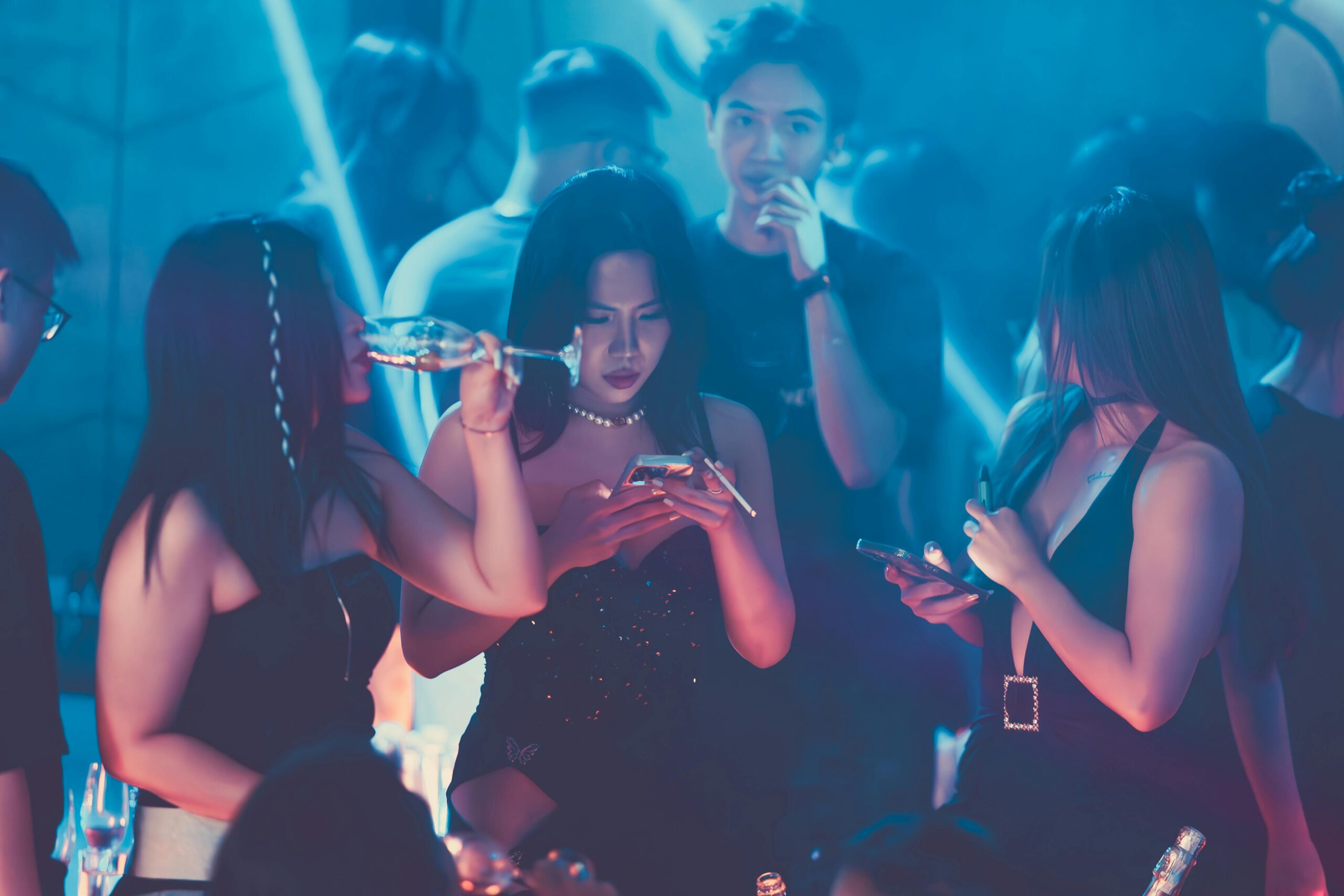 Illustration of A group of people standing around a table with cell phones for the article titled Club Hopping Chronicles: A Nightlife Guide to the Hottest Clubs in 2024 photographed by Đức Trung Đào
